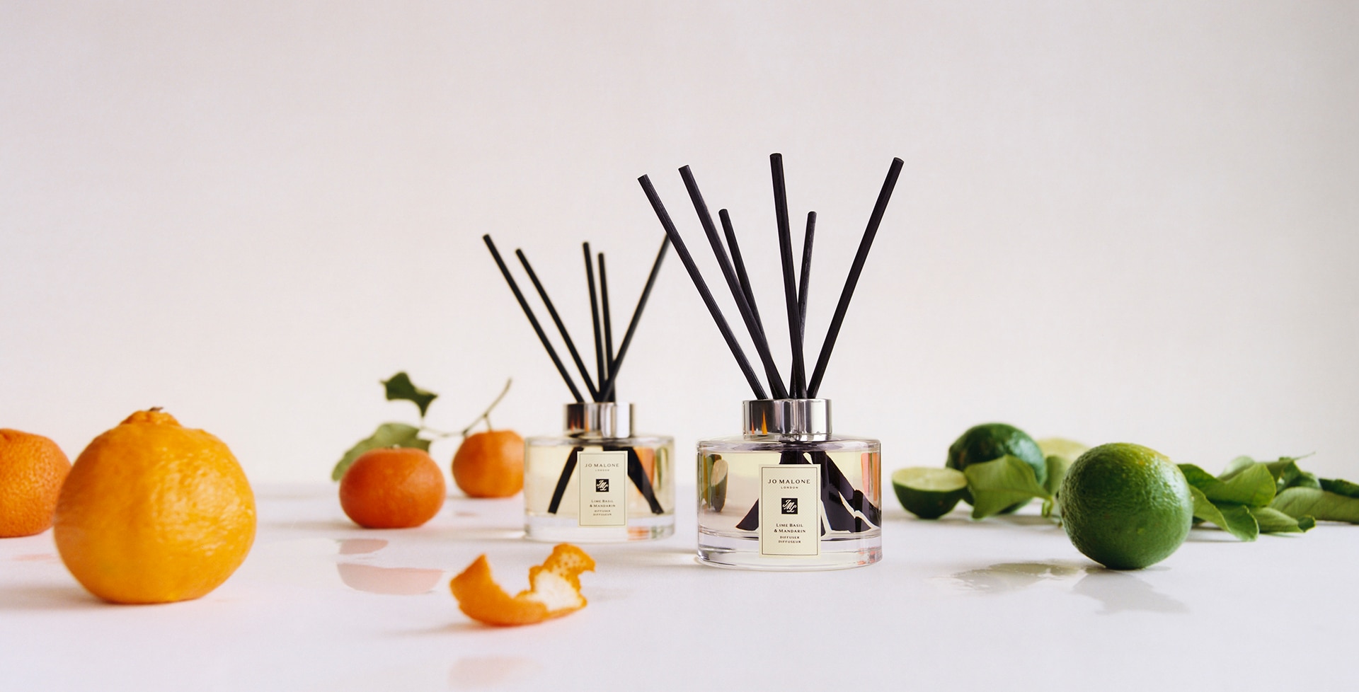 Jo Malone London Lime Basil & Mandarin Diffuser surrounded by oranges and limes