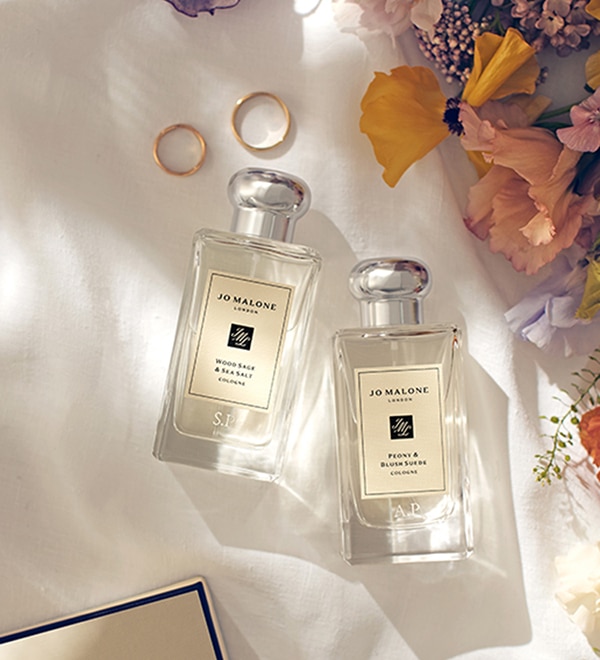 Jo Malone London Colognes engraved with initials, surrounded by flowers and two wedding rings 